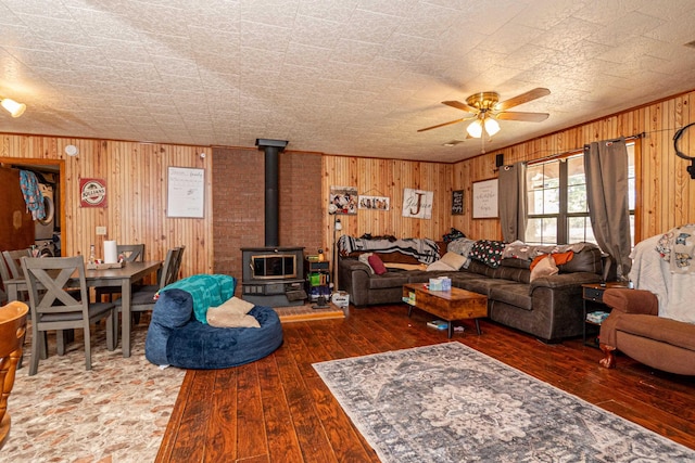 living area with hardwood / wood-style floors, wood walls, a wood stove, and stacked washer / drying machine