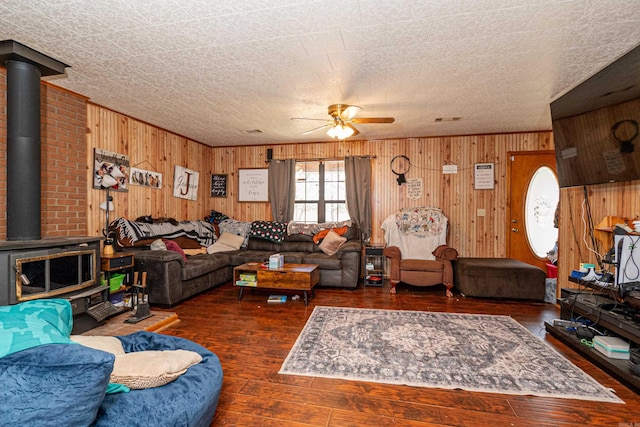 living room featuring wood-type flooring, visible vents, a ceiling fan, a wood stove, and wooden walls