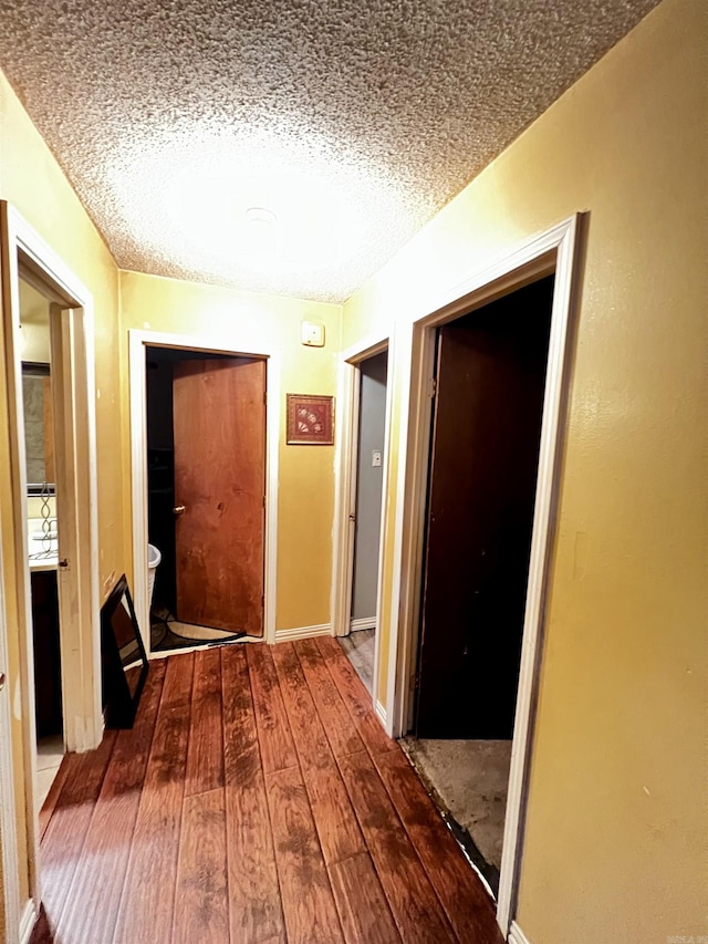 corridor featuring wood-type flooring, a textured ceiling, and baseboards