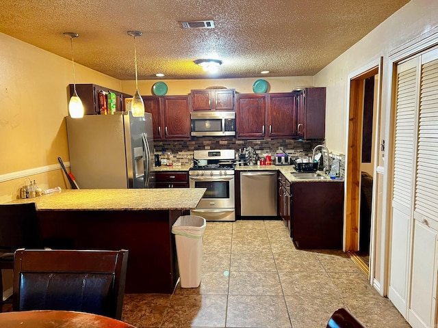 kitchen featuring appliances with stainless steel finishes, a peninsula, light countertops, pendant lighting, and a sink