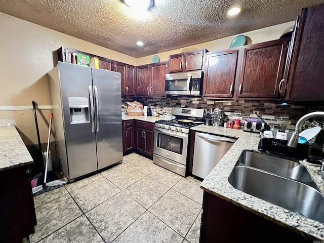 kitchen featuring light stone counters, tasteful backsplash, appliances with stainless steel finishes, a sink, and a textured ceiling