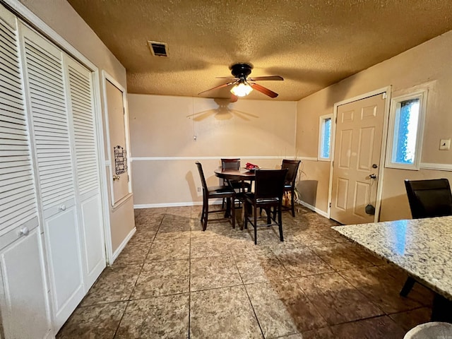 dining area with a textured ceiling, baseboards, visible vents, and a ceiling fan