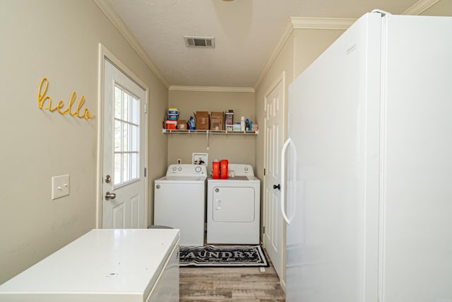 clothes washing area featuring visible vents, ornamental molding, wood finished floors, washer and dryer, and laundry area