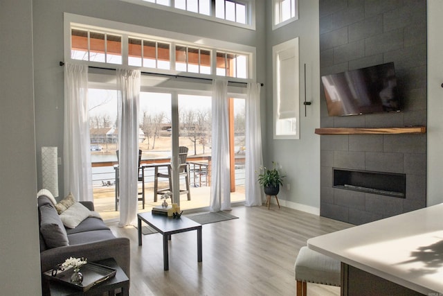 living room featuring a high ceiling, a fireplace, wood finished floors, and baseboards