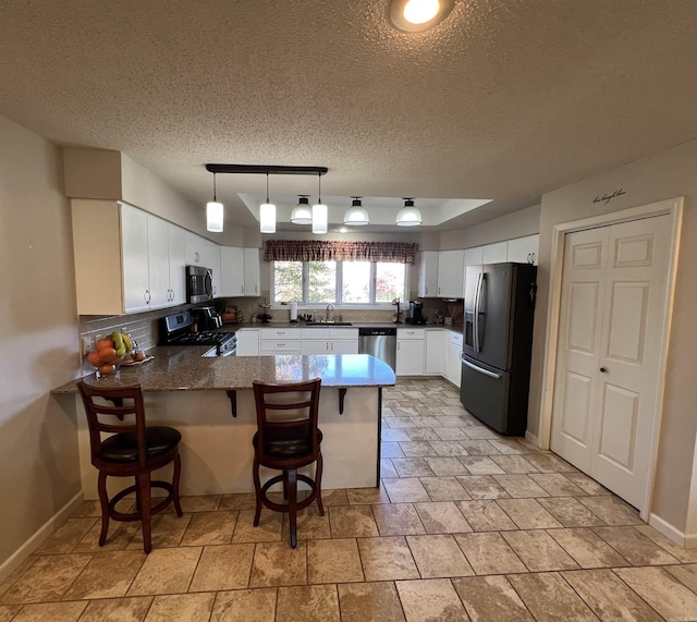 kitchen with a peninsula, a sink, white cabinets, appliances with stainless steel finishes, and tasteful backsplash