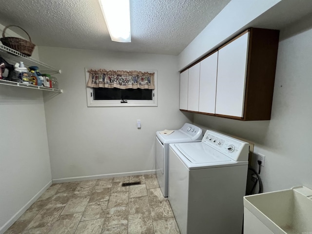 washroom featuring cabinet space, baseboards, washing machine and clothes dryer, a textured ceiling, and a sink