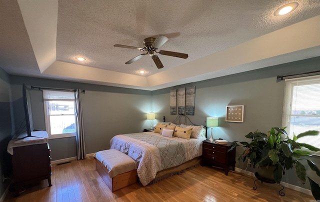 bedroom featuring a tray ceiling, multiple windows, visible vents, and hardwood / wood-style flooring