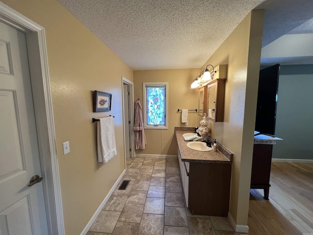 bathroom featuring visible vents, baseboards, a textured ceiling, and vanity