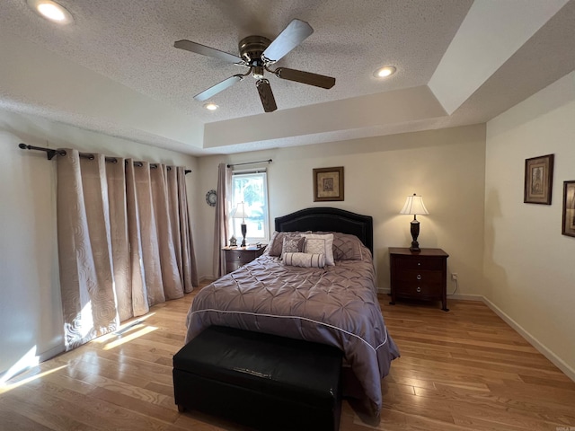 bedroom featuring a textured ceiling, baseboards, a raised ceiling, and light wood-style floors