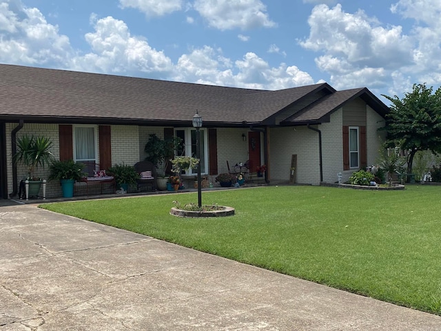 ranch-style home featuring a front yard, brick siding, and roof with shingles