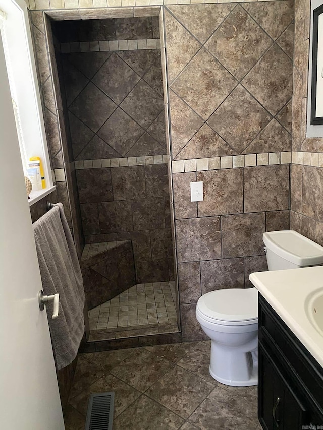 full bathroom with toilet, vanity, visible vents, tile walls, and a tile shower