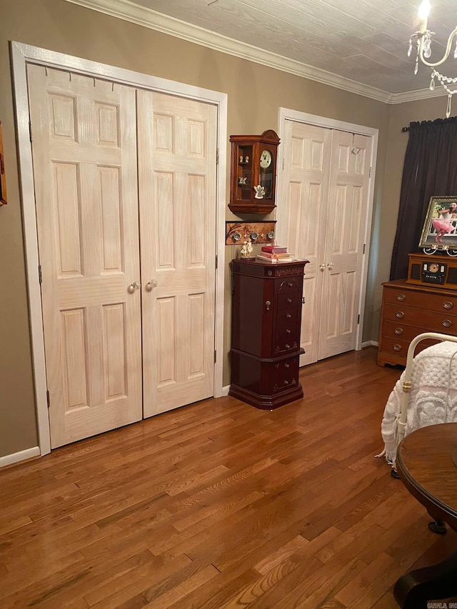 bedroom featuring wood finished floors, crown molding, an inviting chandelier, and two closets