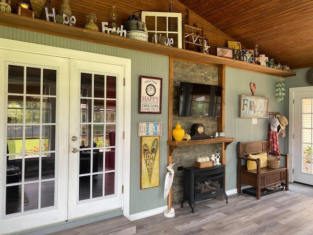 living area with french doors, lofted ceiling, a wood stove, wood finished floors, and baseboards