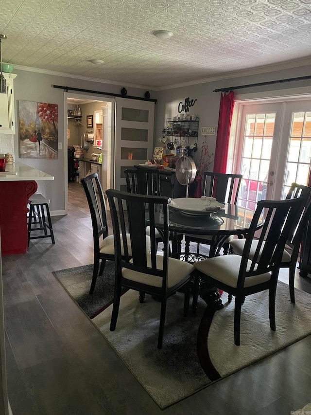 dining area featuring french doors, ornamental molding, a barn door, and wood finished floors