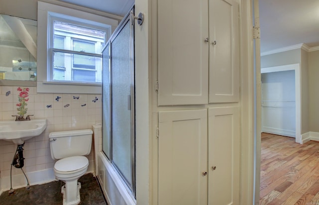 bathroom with toilet, ornamental molding, wood finished floors, combined bath / shower with glass door, and a sink