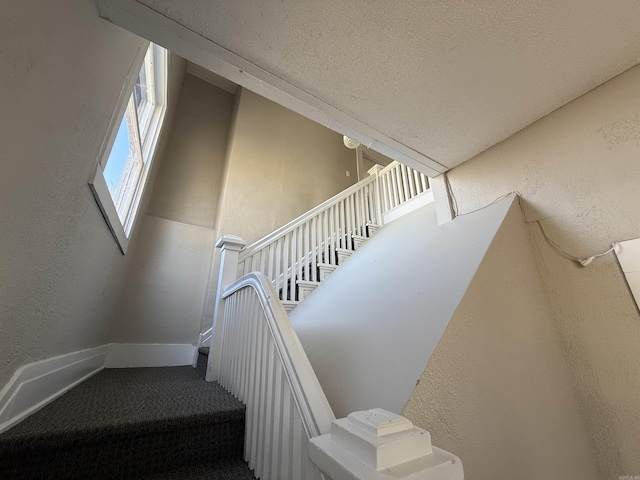 stairs with a textured ceiling, a textured wall, carpet floors, and baseboards