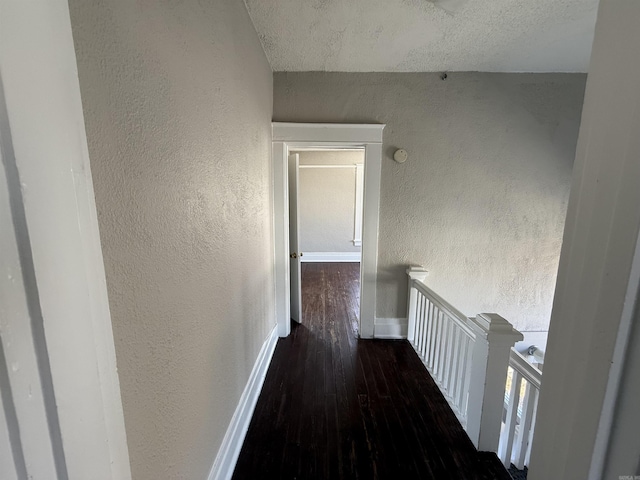 hallway with an upstairs landing, a textured wall, baseboards, and wood finished floors