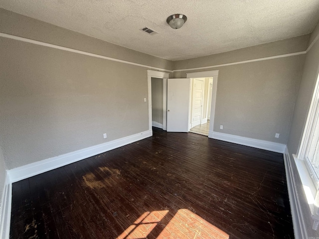 spare room with dark wood-style floors, visible vents, a textured ceiling, and baseboards