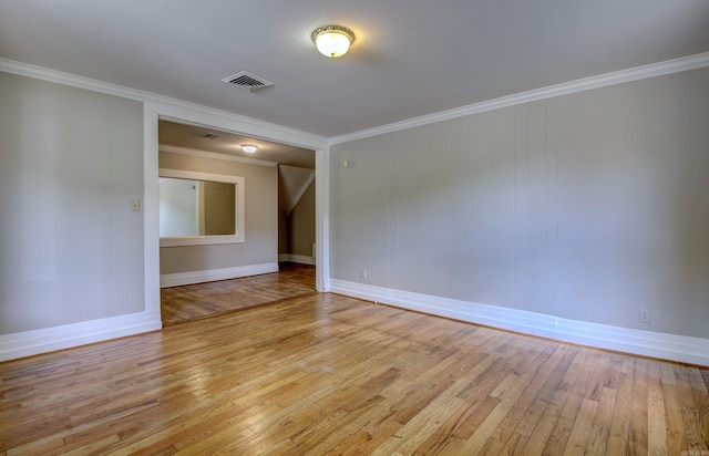 spare room featuring light wood finished floors, baseboards, visible vents, and crown molding