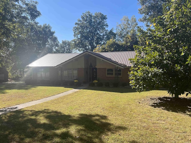 view of front facade featuring metal roof, brick siding, a front lawn, and a standing seam roof