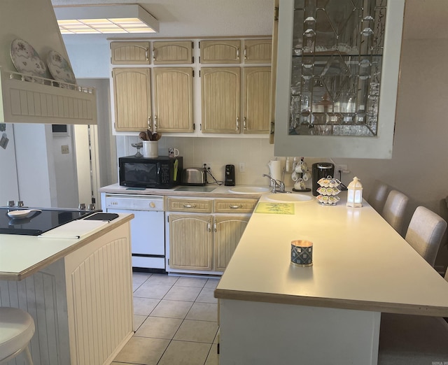 kitchen with light tile patterned floors, a peninsula, a breakfast bar, light countertops, and black appliances