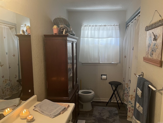 full bathroom with a textured wall, wood finished floors, toilet, and baseboards