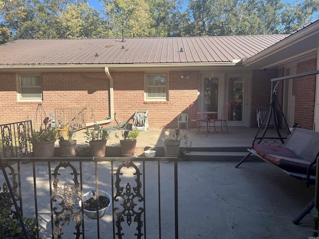 back of house featuring metal roof, brick siding, and a patio