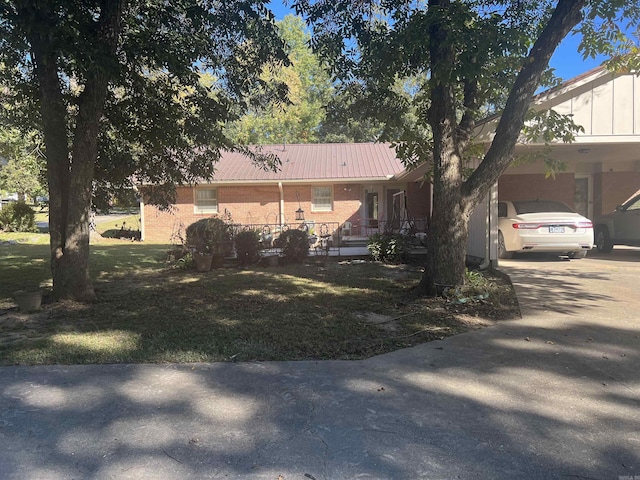 view of front of property featuring metal roof, covered porch, brick siding, concrete driveway, and a front lawn