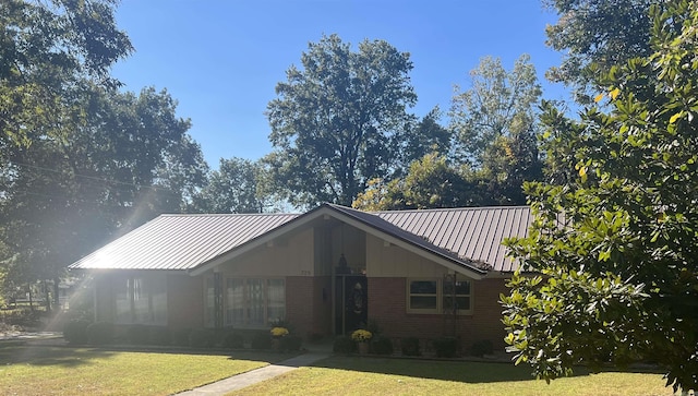 view of front of house featuring a standing seam roof, a front yard, metal roof, and brick siding