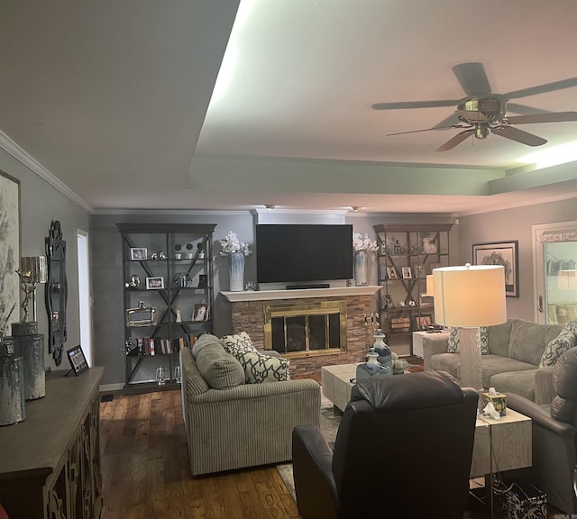 living area featuring ornamental molding, ceiling fan, a stone fireplace, and dark wood finished floors