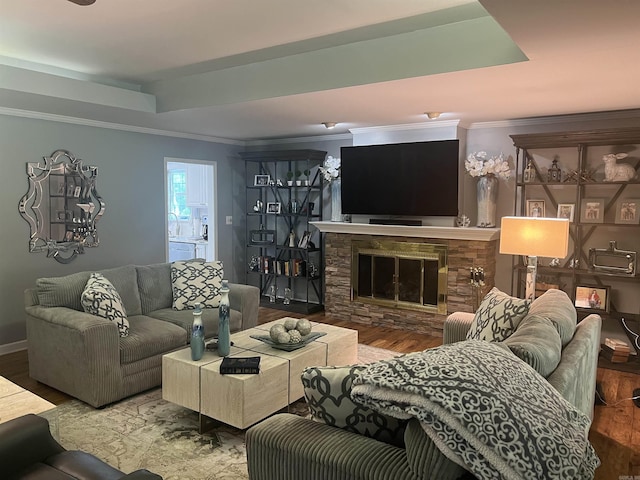 living area featuring ornamental molding, a tray ceiling, a stone fireplace, and wood finished floors