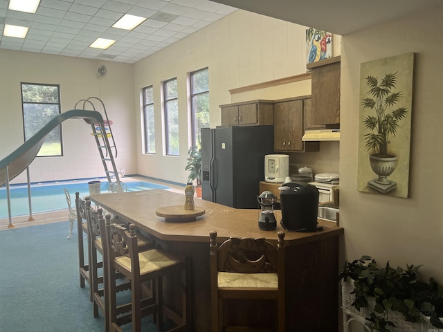 kitchen featuring carpet floors, fridge with ice dispenser, a paneled ceiling, and under cabinet range hood