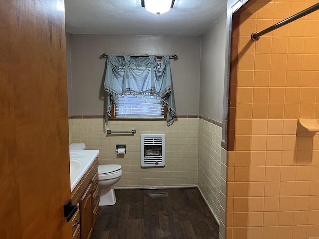 full bath with tile walls, heating unit, toilet, vanity, and wood finished floors