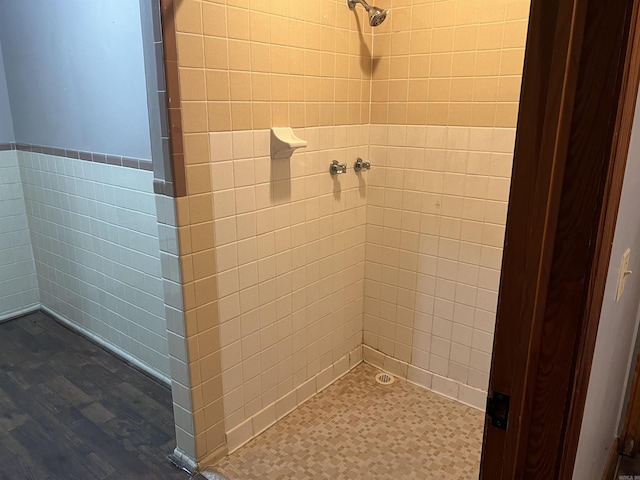 bathroom featuring a tile shower, tile walls, and wainscoting