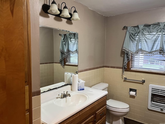 half bath featuring toilet, a wainscoted wall, heating unit, vanity, and tile walls