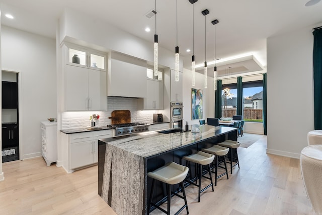 kitchen featuring visible vents, a kitchen breakfast bar, a sink, custom exhaust hood, and backsplash