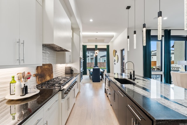 kitchen featuring stainless steel gas stovetop, backsplash, a sink, dark stone countertops, and wall chimney exhaust hood