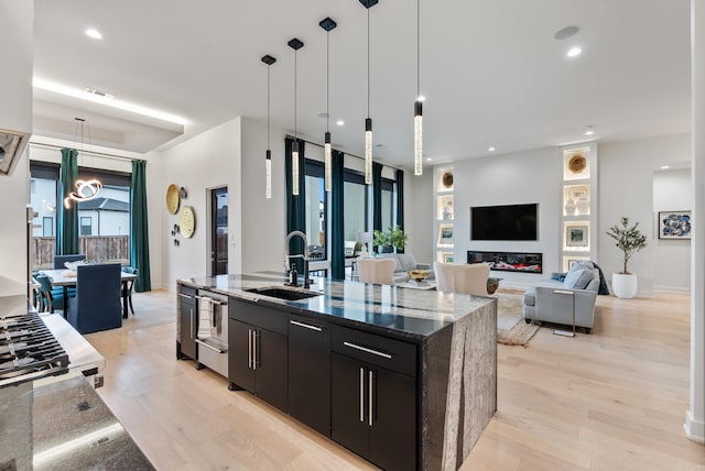 kitchen featuring visible vents, light wood-style floors, a sink, an island with sink, and dark cabinetry