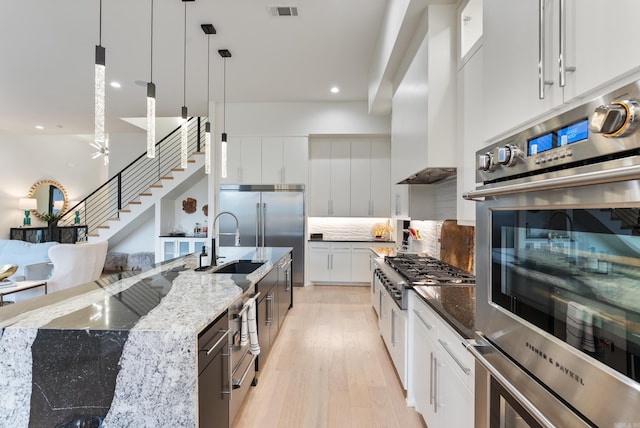 kitchen with stainless steel appliances, visible vents, light wood-style flooring, wall chimney range hood, and dark stone counters