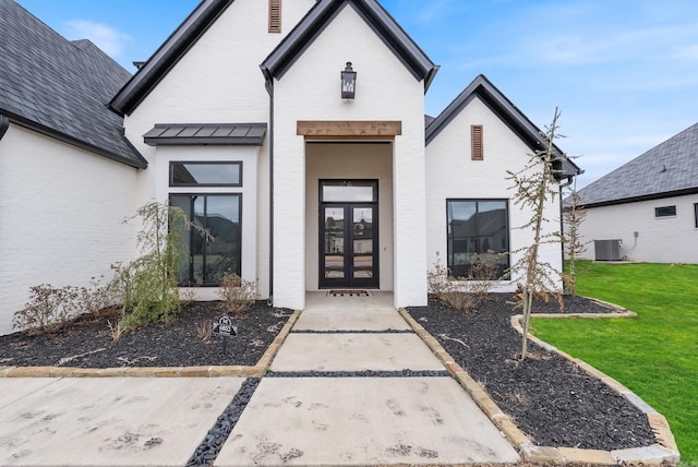 entrance to property featuring french doors, brick siding, a yard, a standing seam roof, and cooling unit