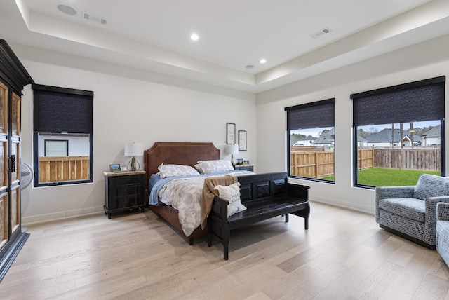 bedroom with light wood finished floors, a raised ceiling, visible vents, and baseboards