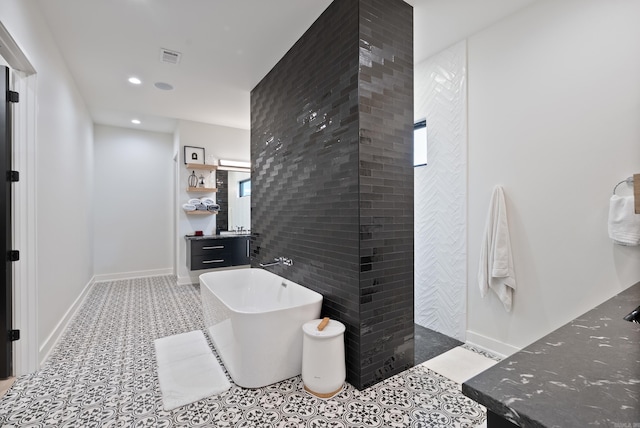 full bath with tile walls, recessed lighting, a freestanding bath, vanity, and tile patterned flooring