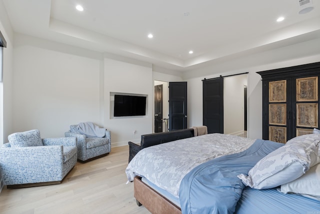 bedroom with light wood-style floors, a barn door, a raised ceiling, and recessed lighting