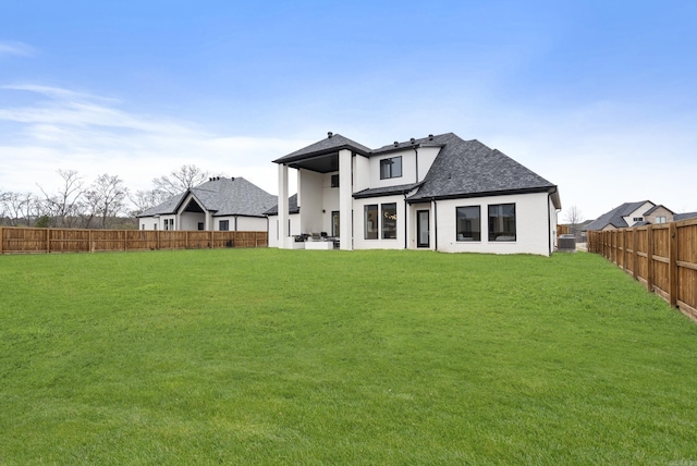 back of house featuring a yard, roof with shingles, and a fenced backyard