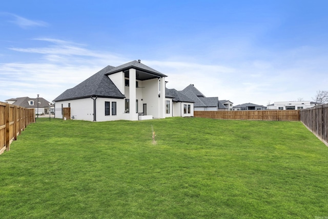 rear view of property with stucco siding, a fenced backyard, a lawn, and roof with shingles