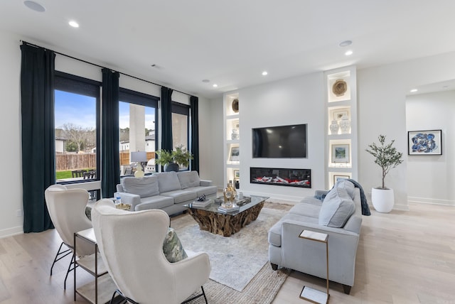 living room featuring light wood-style floors, a glass covered fireplace, baseboards, and recessed lighting