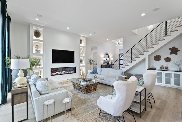 living room with light wood finished floors, recessed lighting, stairs, and a glass covered fireplace