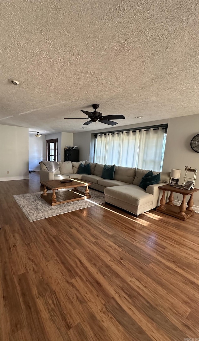 unfurnished living room featuring a textured ceiling, wood finished floors, and baseboards