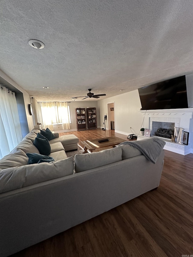 living area with a fireplace with raised hearth, ceiling fan, a textured ceiling, and wood finished floors