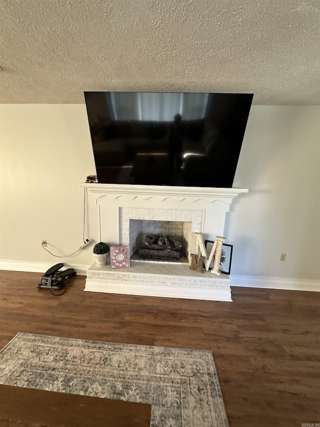 interior details featuring a brick fireplace, a textured ceiling, baseboards, and wood finished floors